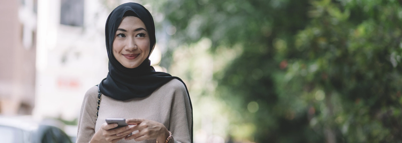 Wanita muda berhijab memegang telefon sambil tersenyum, mencerminkan kesedaran tentang kesihatan wanita seperti kanser rahim.